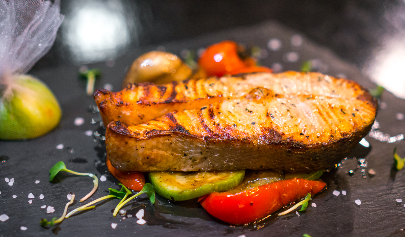 Grilled barramundi fillet presented on a slate serving plate, showcasing its charred, golden exterior.