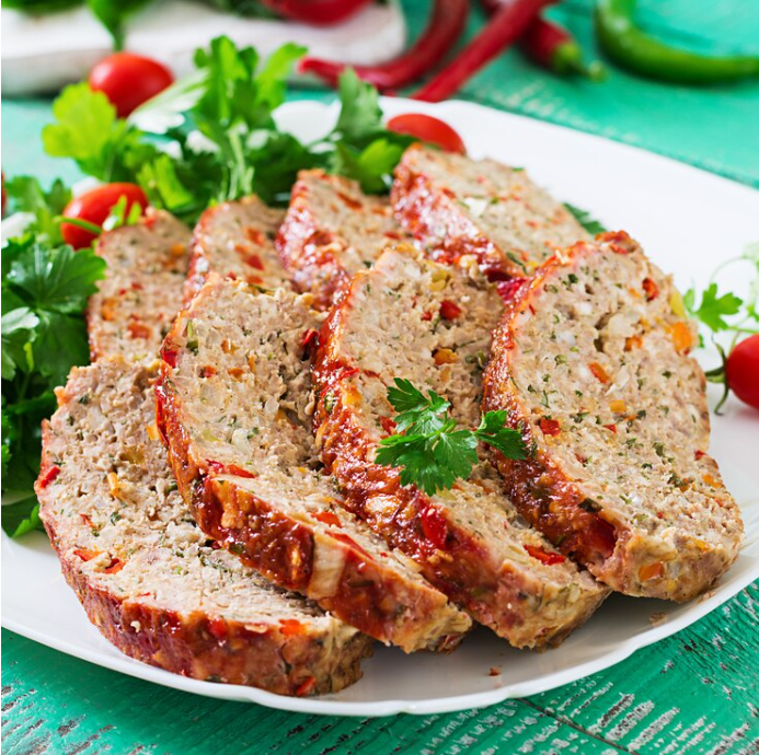 Savory Italian meatloaf sliced and served on a white platter, garnished with fresh parsley, with cherry tomatoes and green herbs in the background, indicating a fresh, homemade recipe perfect for family dinners.
