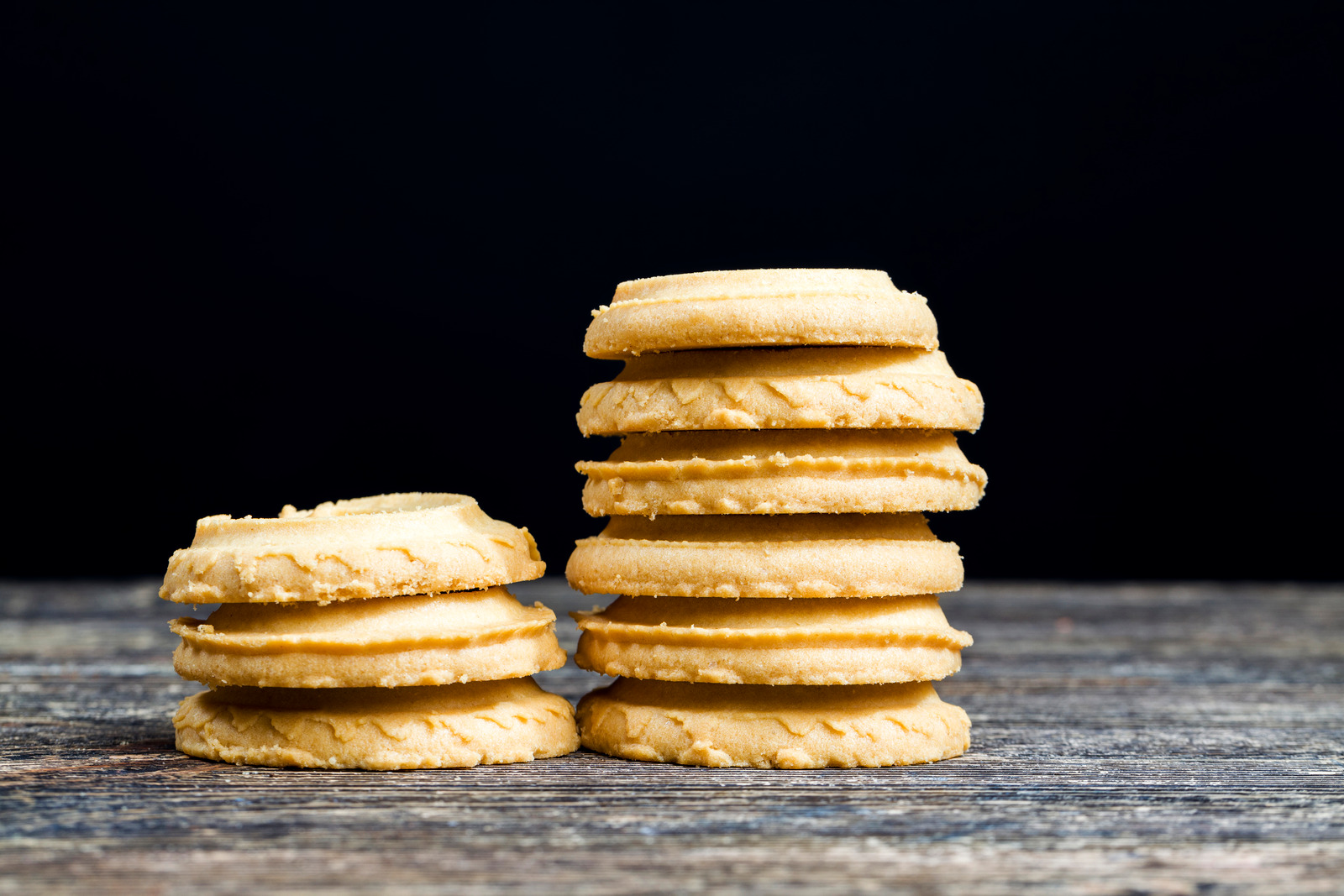 A stack of golden-brown crumbl cookies on a rustic wooden surface against a dark background